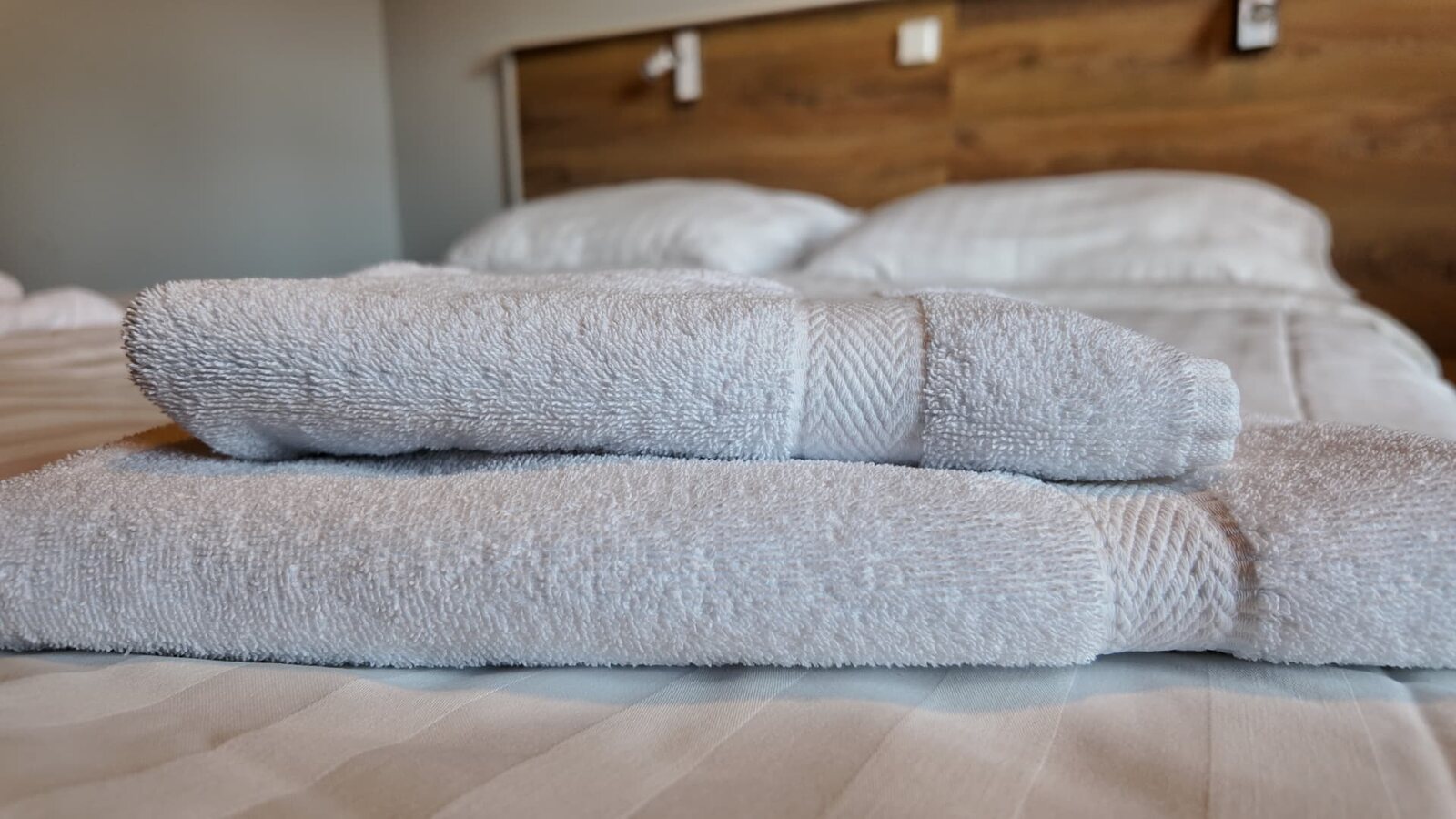 Siististi rullatut valkoiset pyyhkeet sängyllä Peltohovin hotellihuoneessa.